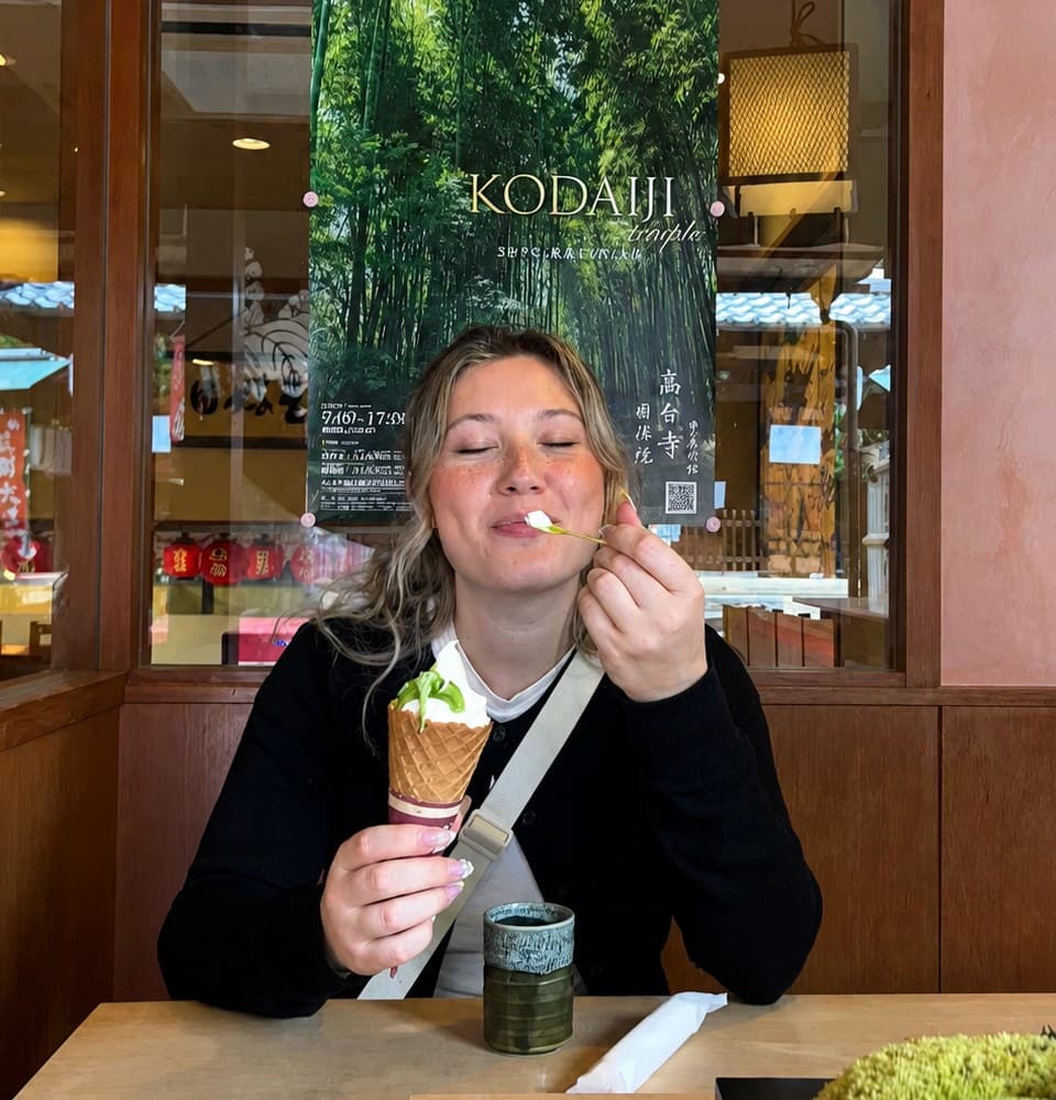 Une femme goûte une glace au matcha dans un salon de thé, une affiche du temple Kōdai-ji derrière elle