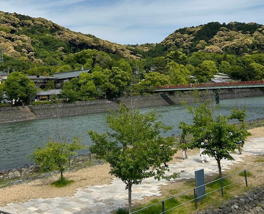 La rivière Uji au pied de collines boisées, un pont rouge et des maisons de thé sur la rive